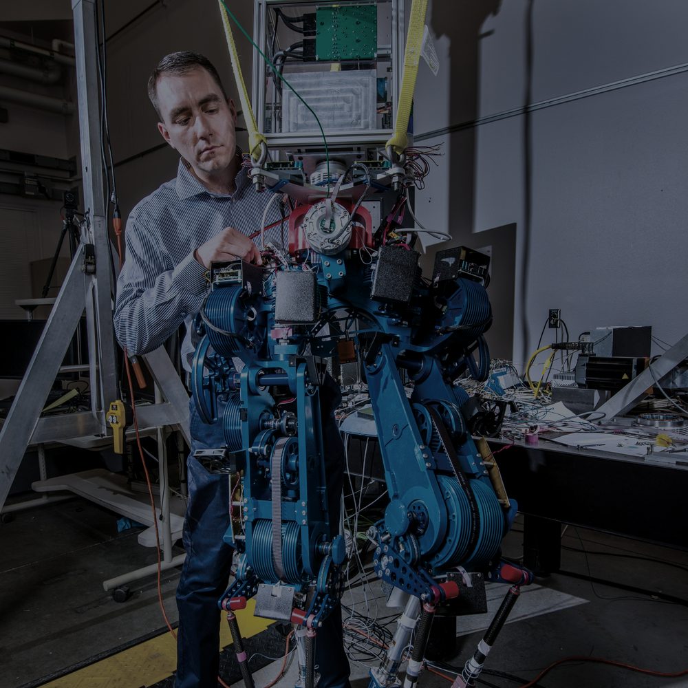 Engineer adjusting the leg actuators of a bipedal research robot in a lab